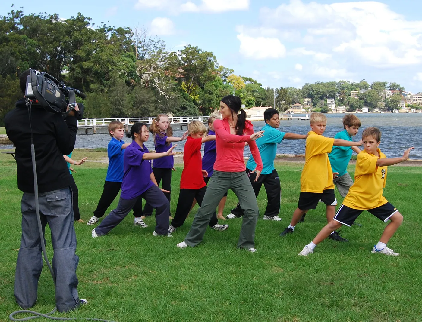 A television camera operator filming a group of children practising tai chi outdoors
